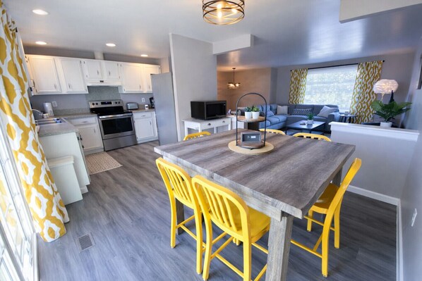 A modern kitchen with white cabinets, a built-in oven, and a dining area with a wooden table and yellow chairs.