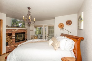 A bedroom with a large bed, a fireplace, and a chandelier.