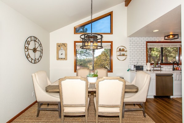 A dining area with a wooden table and four chairs, a chandelier, and a clock on the wall.
