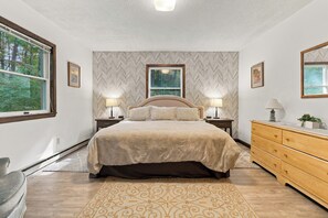 A bedroom with a large bed, two bedside lamps, a dresser, and a window with a view of trees. - Private Wooded Retreat close to Cornell (Freeville)