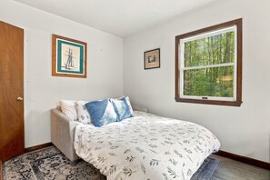 A bedroom with a bed, a window, and two framed pictures on the wall.