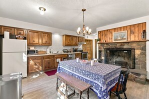 A kitchen with wooden cabinets, a stone fireplace, and a dining area with a table and bench.
