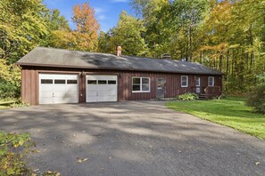 A two-story wooden house with a garage, a front porch, and a driveway. - Private Wooded Retreat close to Cornell (Freeville)