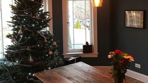 A room with a Christmas tree, a wooden table, and a window with a view of the outside. - The Greenleaf House—Whole House (Chicago)