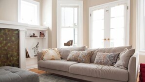 A living room with a beige sofa, patterned cushions, a red chair, a white bookshelf, and a brick wall. - The Greenleaf House—Whole House (Chicago)