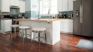 A kitchen with white cabinets, a stainless steel refrigerator, a built-in oven, and a bar area with stools. - The Greenleaf House—Whole House (Chicago)