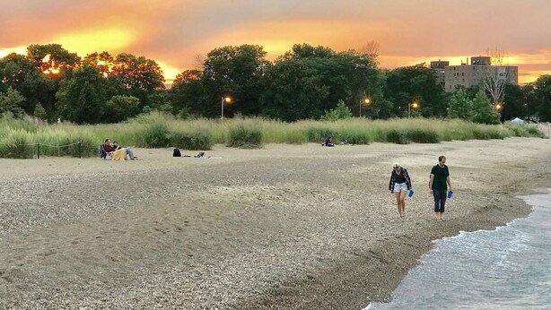 A beach with people walking and sitting, trees in the background, and buildings in the distance. - The Greenleaf House—Whole House (Chicago)