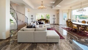 A spacious living room with a large sectional sofa, a dining area with a table and chairs, a staircase, and a chandelier. - Villa Stellare, with private pool and sea views (Capo d'Orlando)