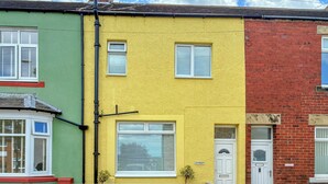 Uma fileira de três casas com cores diferentes: verde, amarelo e vermelho. Cada casa tem uma porta da frente e janelas com persianas.