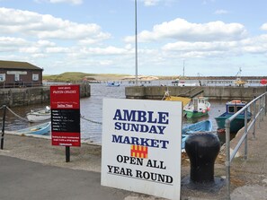 A sign for the Amble Sunday Market, open all year round, with boats docked in the background. - 2 bedroom accommodation in Amble, near Alnwick (Amble, near Alnwick)