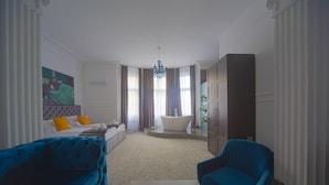 A modern hotel room with a large bed, a sitting area with blue sofas, a bathtub, and a large window with curtains. - Kings Palace Suites (Belgrade)
