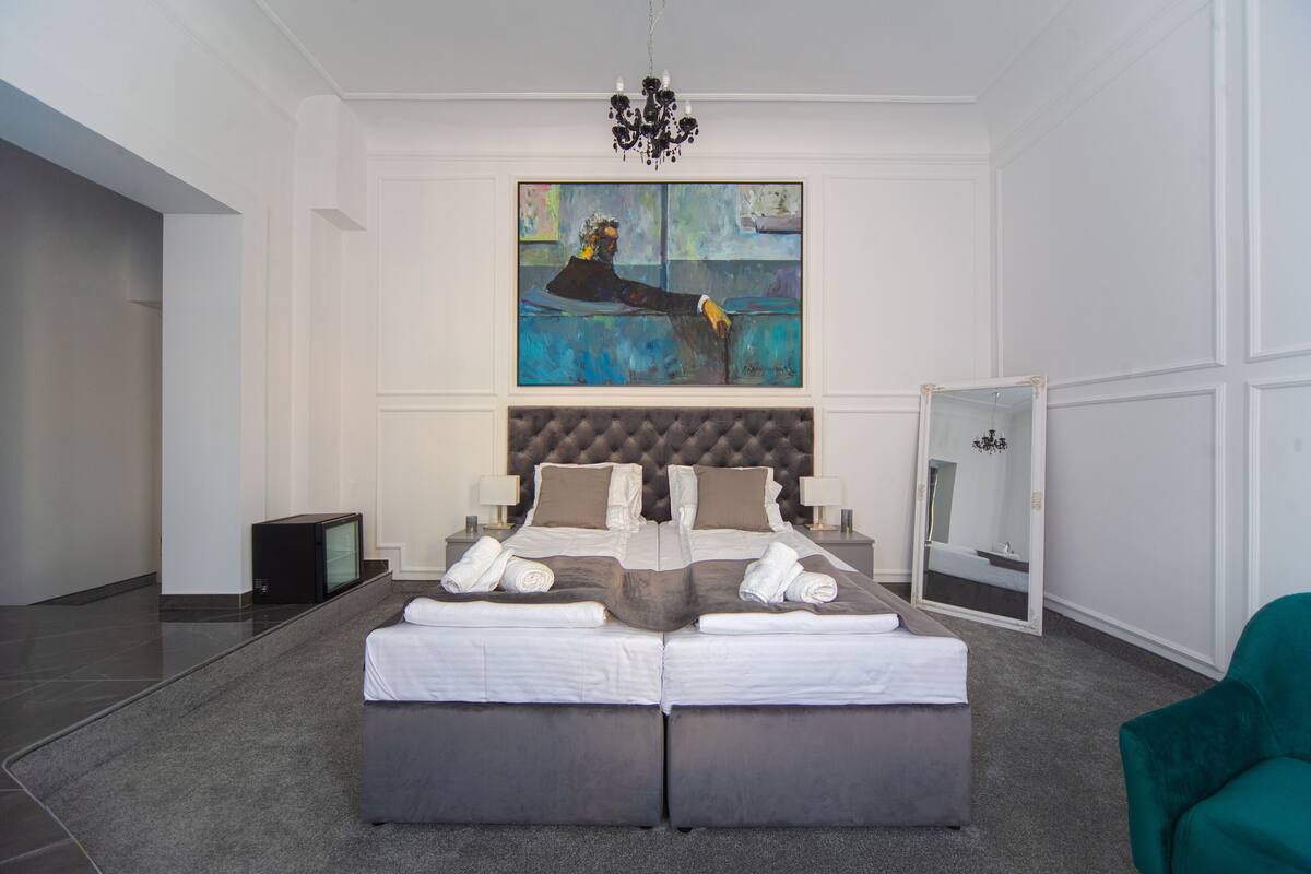 A modern bedroom with a large bed, a painting on the wall, a chandelier, and a mirror.