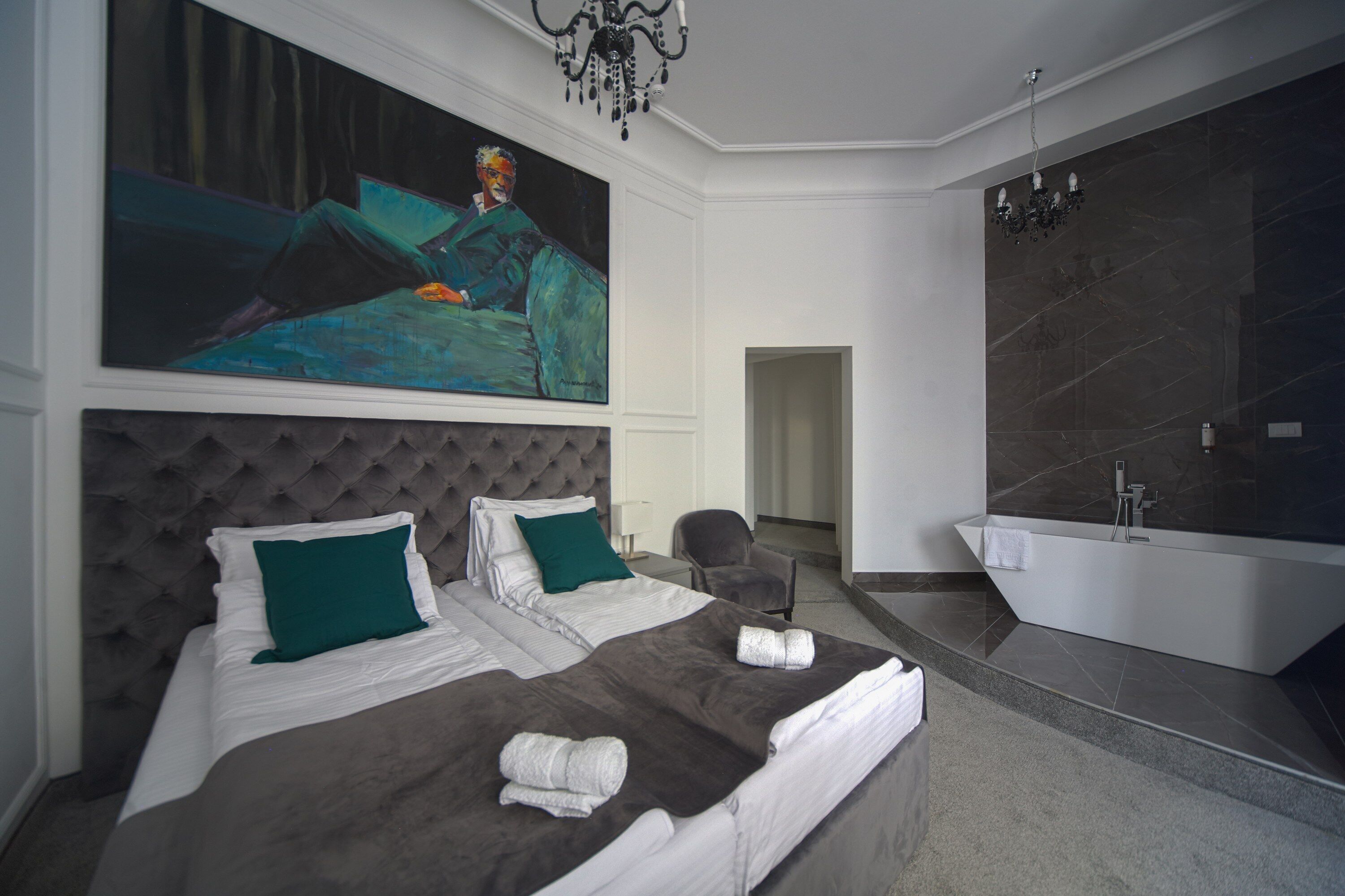 A modern bedroom with a large bed, a painting, a chandelier, a bathroom with a bathtub, and a marble wall.
