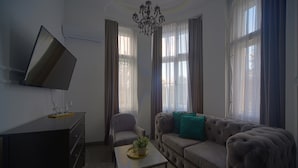 A living room with a sofa, armchair, coffee table, TV, and curtains. - Kings Palace Suites (Belgrade)