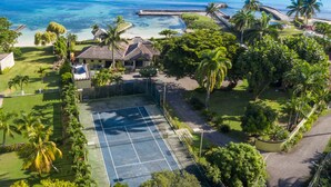 An aerial view of a resort with a tennis court, palm trees, and a beach. - A beautiful private beachfront paradise in Old Fort Bay, Ocho Rios (St. Ann Parish)