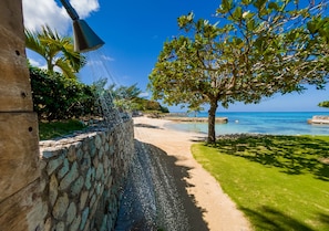 A stone wall with a water feature, a pathway leading to a beach, and a tree with a view of the ocean. - A beautiful private beachfront paradise in Old Fort Bay, Ocho Rios (St. Ann Parish)