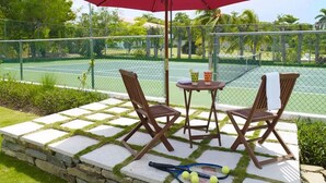 An outdoor seating area with a red umbrella, two wooden chairs, a small table, and a tennis racket on a stone-tiled surface. - A beautiful private beachfront paradise in Old Fort Bay, Ocho Rios (St. Ann Parish)