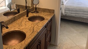 Ein Badezimmer mit einer Granitplatte, zwei Waschbecken, einem großen Spiegel und einer großzügigen Dusche.