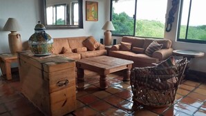 Un salon chaleureux avec un canapé, une table basse en bois, un fauteuil en osier et un vase décoratif.