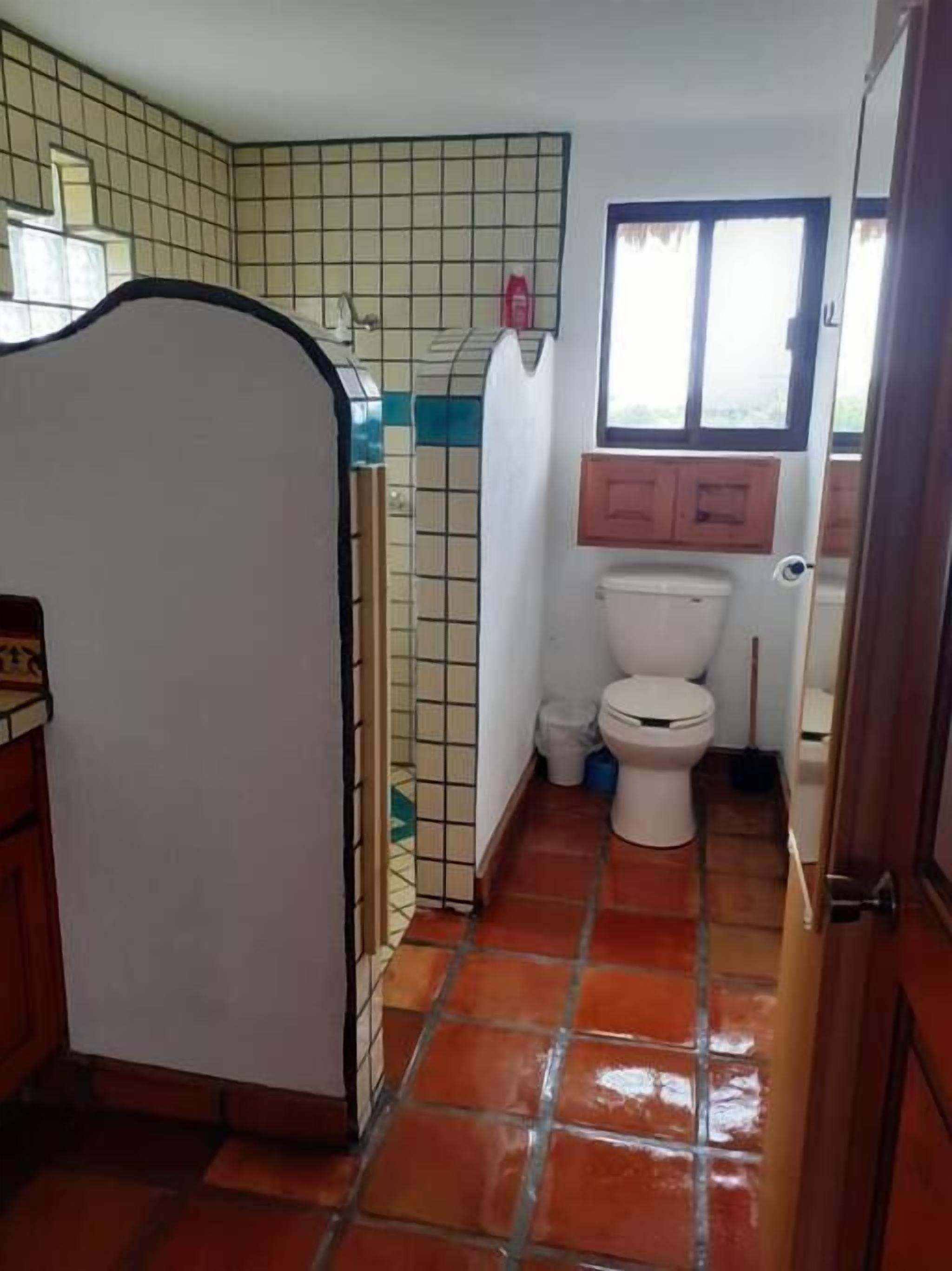 Une petite salle de bain comprenant des toilettes, une petite fenêtre et des murs carrelés.