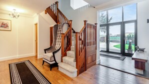 A spacious living area with a wooden staircase, a plush armchair, and a large window offering a view of the outdoors.