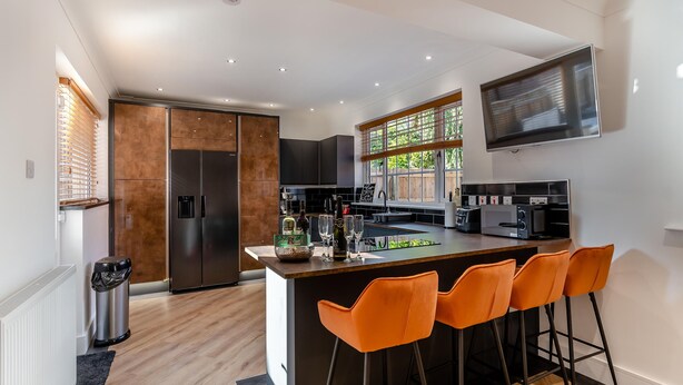 A modern kitchen with a central island, bar stools, a large window, and built-in appliances.