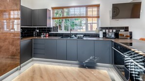 A modern kitchen with dark cabinets, a large window with blinds, and a built-in oven.