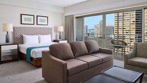 A hotel room with a bed, a sofa, a coffee table, and a balcony with a city view.