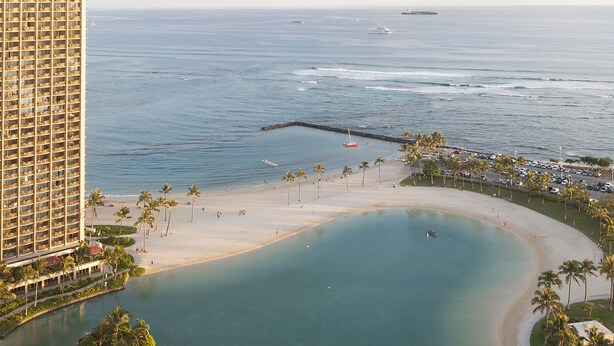 A coastal hotel with a beachfront, a large building, and a calm bay.