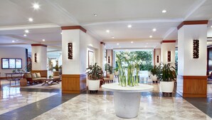 A spacious lobby with a central round table, seating areas, and potted plants.