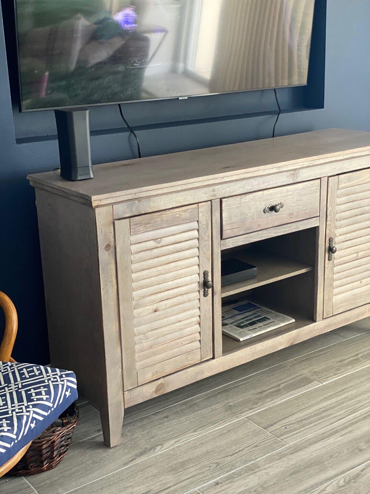 A wooden cabinet with two doors and a shelf, a television on top, and a patterned cushion on the floor.
