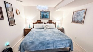 A bedroom with a bed, two bedside tables, a wall clock, and framed pictures. - Hutchinson Haven of Rest (Hutchinson)