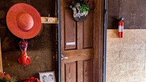 A wooden door with a 'welcome' sign, a red hat, and a table with a red mat and flowers. - Hutchinson Haven of Rest (Hutchinson)