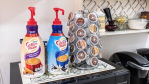 A coffee station with two bottles of coffee creamer, a dispenser of French vanilla creamer, and a stack of coffee pods. - Hutchinson Haven of Rest (Hutchinson)