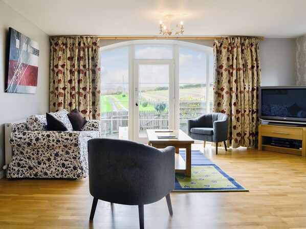 A living room with a sofa, armchair, TV, and a view through a glass door.