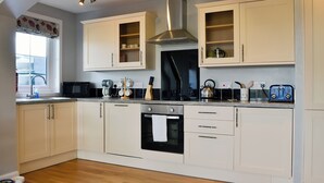 A kitchen with white cabinets, a black stove, and a window with a floral valance.