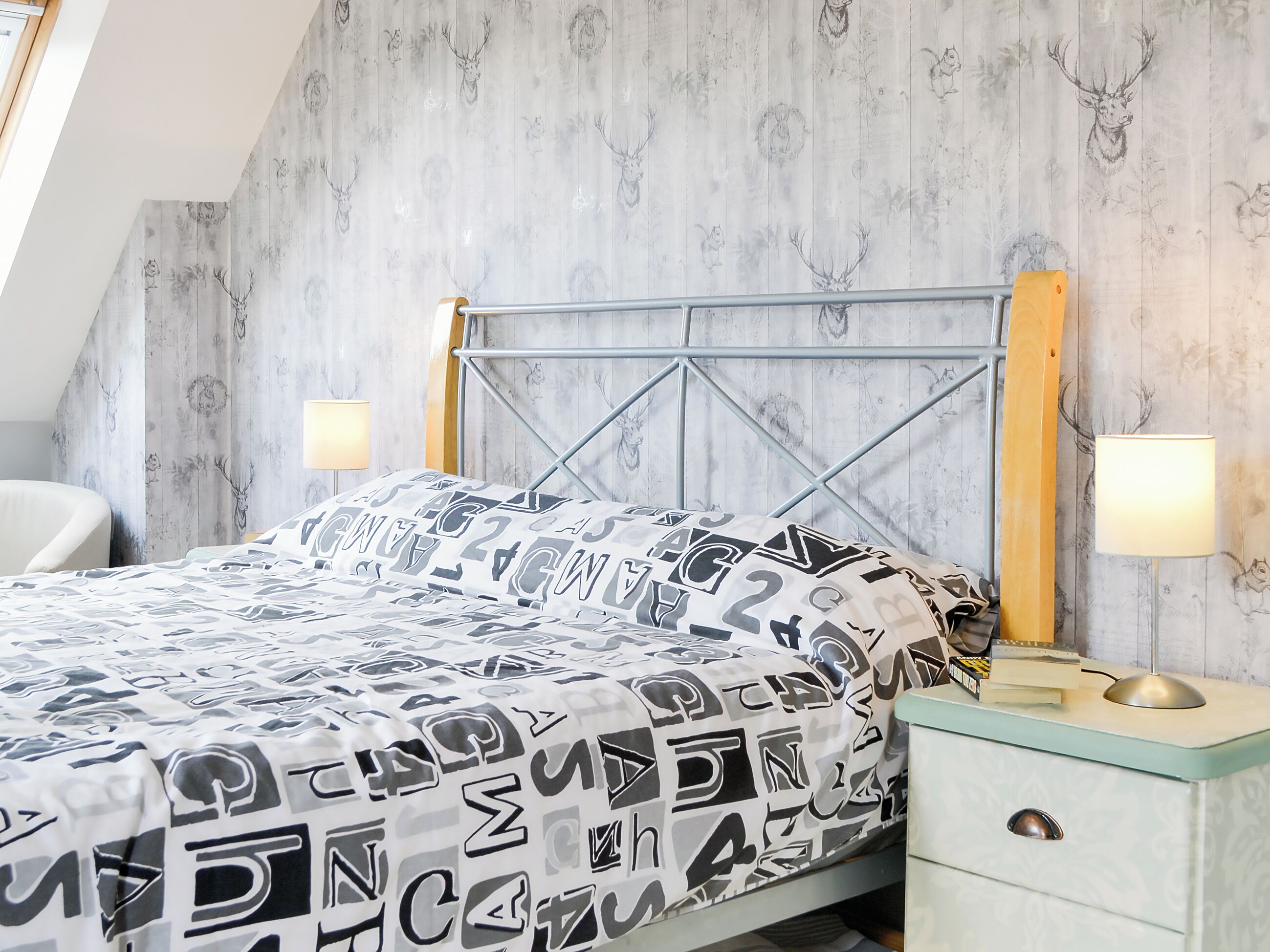 A bedroom with a bed, a nightstand, a lamp, and a chair.