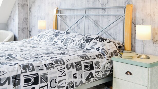 A bedroom with a bed, a nightstand, a lamp, and a chair.