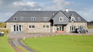 A stone house with a grey roof, a driveway, and a car parked in front.