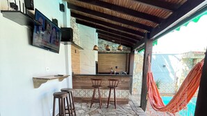 Un espacio al aire libre cubierto con piso de piedra, taburetes de madera, una encimera de cocina y una hamaca.