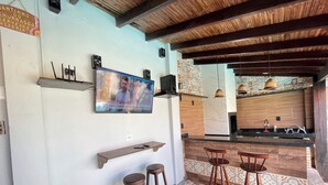Una cocina con techo de madera, un televisor en la pared, piso de baldosas de piedra y una barra con taburetes.