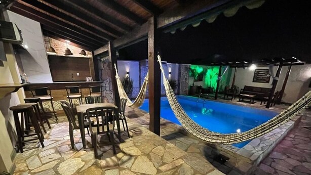 Un área de piscina al aire libre con suelo de piedra, una hamaca y una zona de bar.