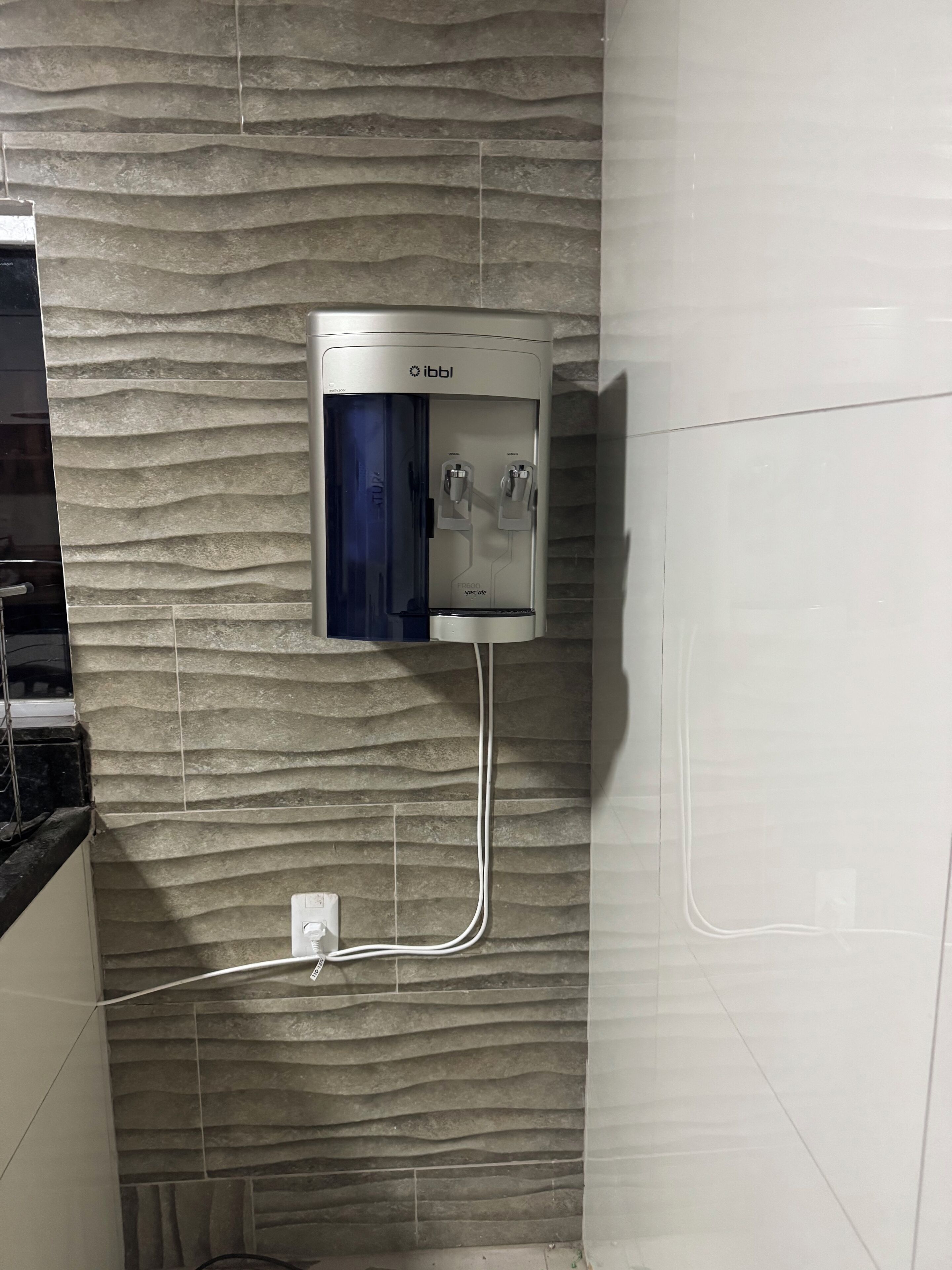 En vattenautomat som är monterad på en vägg med en strukturerad yta, och ett eluttag sitter under den.