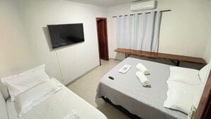 Habitación de hotel con dos camas individuales, un televisor de pantalla plana montado en la pared, un banco de madera y un equipo de aire acondicionado.