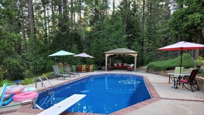 Uma piscina com espreguiçadeiras e guarda-sóis, cercada por árvores.