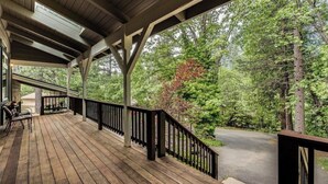 Um deck de madeira com guarda-corpo, com vista para uma estrada e árvores densas.