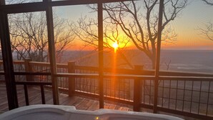 A hot tub with a view of the sunset over a body of water, surrounded by a wooden deck and a railing. - Majestic Views, Romantic Brow Home 1.5 Miles From The Heart Of Mentone (Mentone)