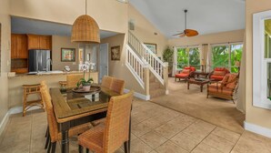 A spacious living area with a dining table, wicker chairs, and a kitchen area with wooden cabinets and a refrigerator. - Regency at Poipu Kai #621 By Parrish Kauai - premier condo with central air grea (Koloa)