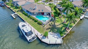 Una casa grande con piscina, un bote amarrado y un muelle pequeño.