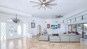 Un salón amplio con un sofá modular gris grande, un ventilador de techo y un televisor en la pared.